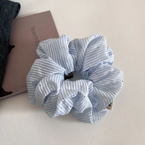 Detail of blue striped scrunchie with sparkling beads on textured white surface