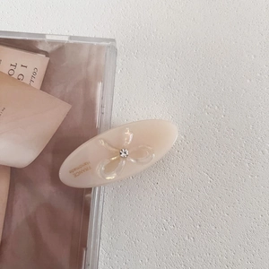 Detail of cream oval hair clip with sparkling crystal bow and gold handmade lettering