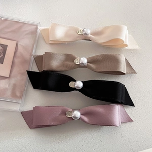 Detail of four colorful layered satin bow hair clips with pearls and metal tags