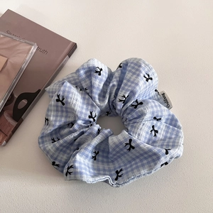 Detail showing blue plaid scrunchie with bird patterns and delicate brand label