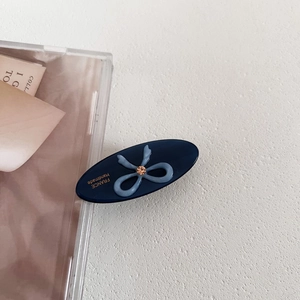 Detail showing the oval blue hair clip with a bow and gold France Handmade lettering