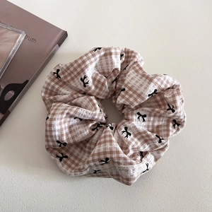 Brown gingham scrunchie with bow patterns on a clean minimalist white surface