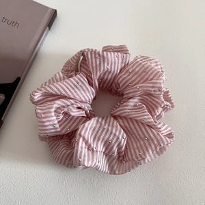 Close-up of pink striped scrunchie with silver micro beads on white textured surface