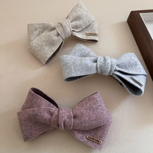 Detail showing the thick wool texture and golden handmade metal tag on the bow hair clip