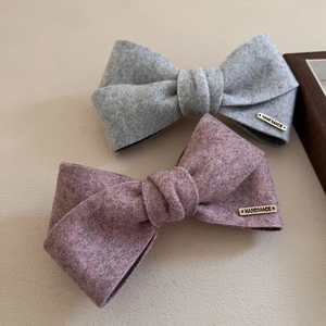 Close-up of soft velvet bow hair clips with handmade metal tag in oat grey and rose colors