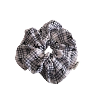 Checkered scrunchie with black bow pattern and white brand label on white background