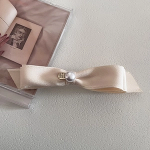Detail of satin bow hair clip with large pearl center and gold love charm pendant