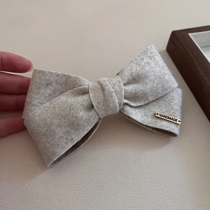 Oatmeal grey flannel bow hair clip with handmade gold tag on beige background