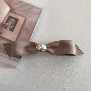 Close-up of champagne satin bow hair clip with pearl detail and gold metal tag