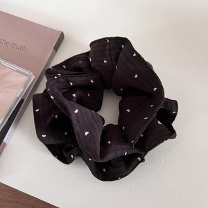 Detailed view of a black scrunchie with white heart patterns on soft ribbed fabric texture