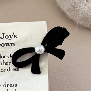 Elegant black velvet bow hair clip with central pearl on card with knit background