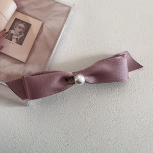 Detail of satin bow hair clip with faux pearl and gold heart tag on a cream background