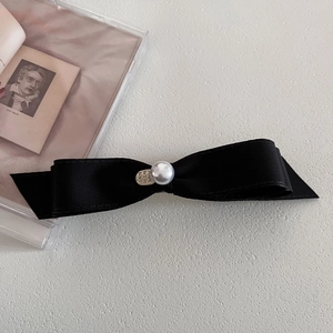 Detail of black satin bow hair clip featuring a white pearl and silver heart tag