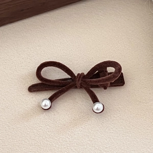 Detail of a brown velvet bow hair clip with elegant white pearls on a textured background