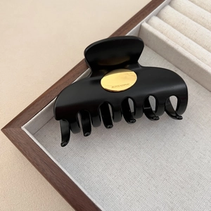 Matte black claw clip with gold France Handmade logo on a beige display tray