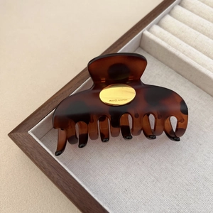 Detail of the golden metal logo plate and tortoiseshell texture on the hair claw clip