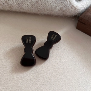 Detail view of two dark brown acetate bow hair clips with gold handmade lettering