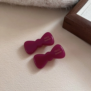 Close-up of burgundy acetate bow hair clips with gold handmade lettering detail