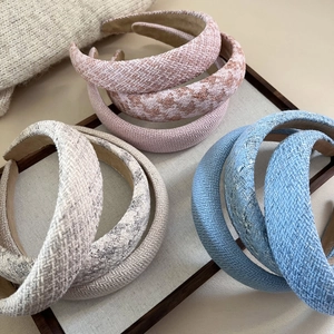 Close-up of three tweed plaid headbands in pink, blue and grey on a linen tray