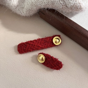 Close-up of red tweed oval hair clips with gold buttons and woven texture finish