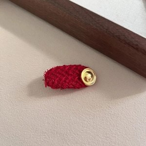 Detailed view of red tweed oval hair clip with vintage golden button and woven texture
