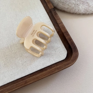Détail de la pince à cheveux en acétate crème avec logo sur un plateau en bois