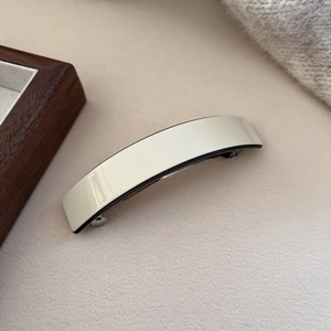 Close-up of elegant cream acetate hair clip with silver spring clasp on textured background