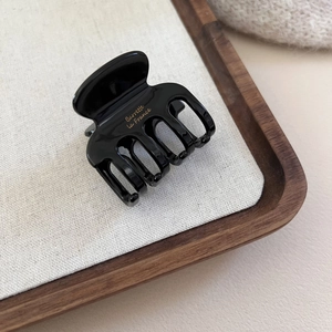 Détail de la pince à cheveux noire en acétate avec texte doré sur texture de lin chic