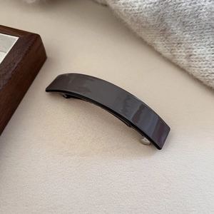 Detail of dark grey acetate hair clip with premium glossy finish on beige background