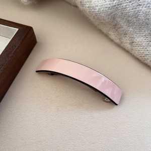 Detail of light pink acetate hair clip with black edges on warm beige background
