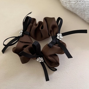 Détail d'un chouchou en satin avec des nœuds en strass brillants et texture de tissu marron
