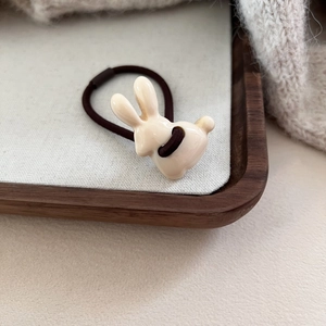 Détail d'un élastique à cheveux lapin crème sur plateau bois et décor tricoté