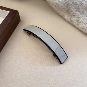 Detailed view of grey acetate hair clip with black border on a warm beige background