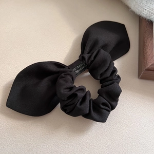 Detail of a handmade black bow scrunchie with a visible handmade tag and textured fabric