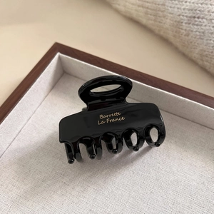 Elegante pinza per capelli in acetato nero con scritte dorate su vassoio in lino crema