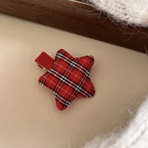 Close-up of red and black buffalo plaid star hair clip on soft beige plush background