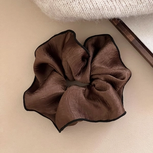 Close-up of a large brown satin scrunchie with elegant black contrast piping and soft texture