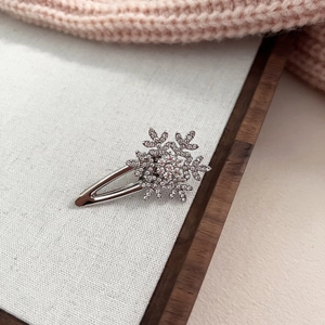 Détail d'une pince à cheveux flocon de neige argentée avec strass sur fond blanc doux