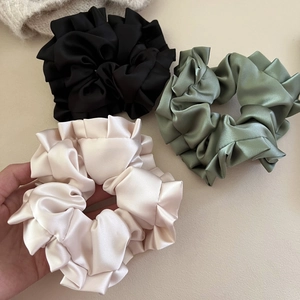 Detailed macro view of large satin pleated scrunchies in black, green, and champagne silk fabric