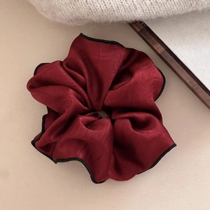 Detail of burgundy satin scrunchie with black trim showing silk texture and ruffles