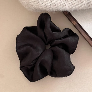Detail of a black satin large scrunchie with contrast edge on beige knit fabric