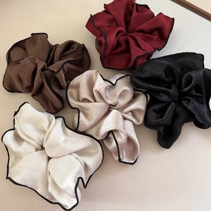 Detail view of five large satin scrunchies in assorted colors with black contrast edging