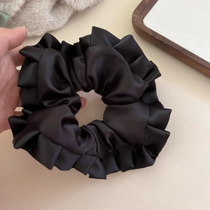 Detailed view of large black satin scrunchie featuring elegant ruffled edges and smooth texture