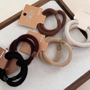 Close-up of five sets of thick ribbed hair bands in earthy tones on a rustic display tray