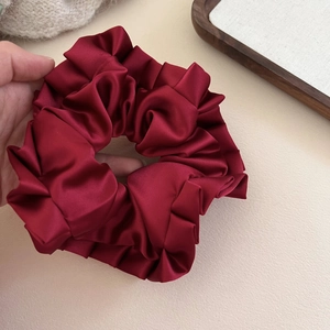 Detail of burgundy satin pleated scrunchie showing glossy texture and elastic stretch