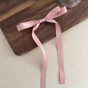 Close-up of soft pink satin ribbon bow hair clip on a textured walnut wood tray