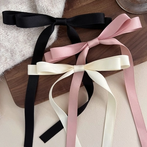 Three satin bow hair clips in black pink and cream displayed on a wooden tray