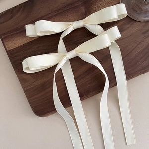 Close-up of cream satin bow hair clips with long streamers on a wooden tray
