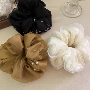 Détail de trois chouchous en organza avec perles en noir, doré et blanc cassé