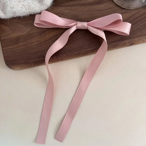 Detailed view of elegant pink satin bow hair clip with long flowing ribbons on wood base